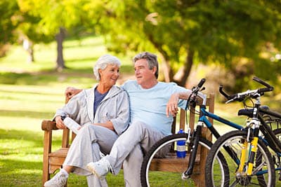 Retired couple riding bikes and sitting on a bench in a continuing care retirement community.